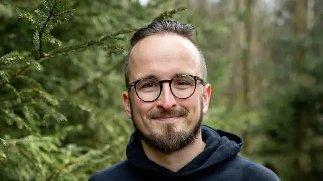 Richard Mai steht mit einem Hoodie mit der Aufschrift SyStep im Wald