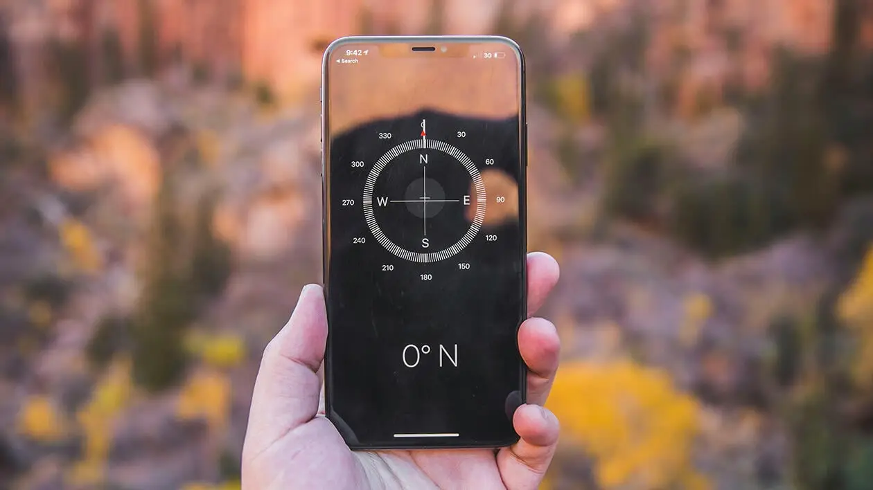 Mann hält Handy mit Kompass-App in der Hand, im Hintergrund ist eine Berglandschaft zu sehen