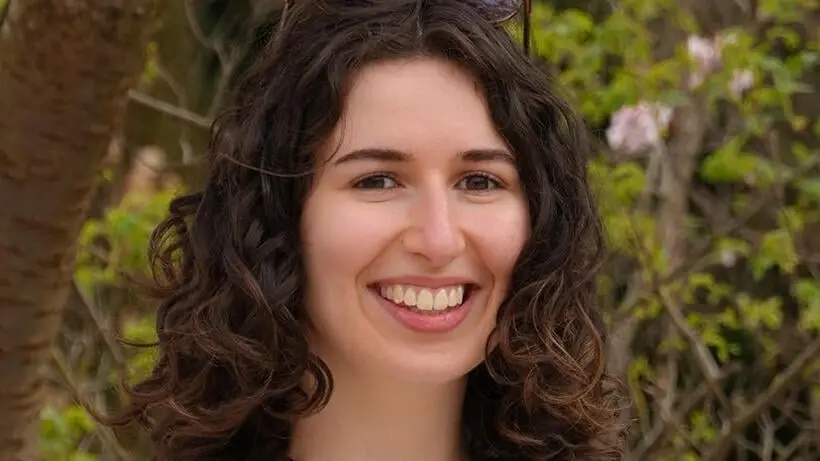 YFU-Ehrenamtliche Israa Kretschmer vor einer Landschaft mit Bäumen und rosa Blüten mit Sonnenbrille auf dem Kopf